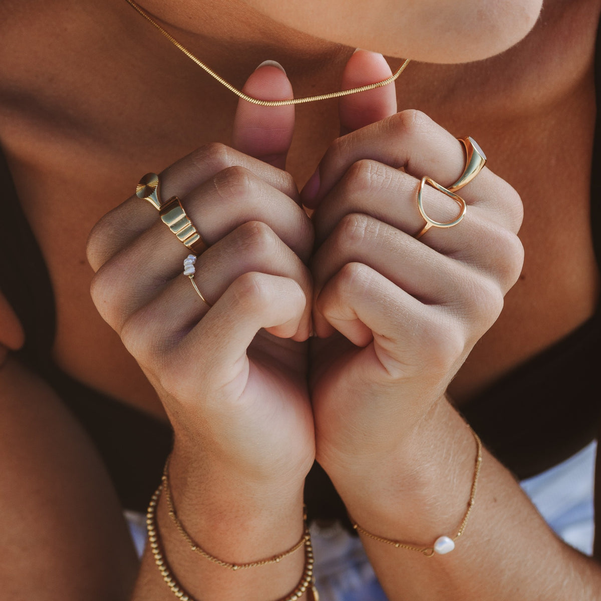 Stacked gold rings and dainty gold bracelets worn on both hands